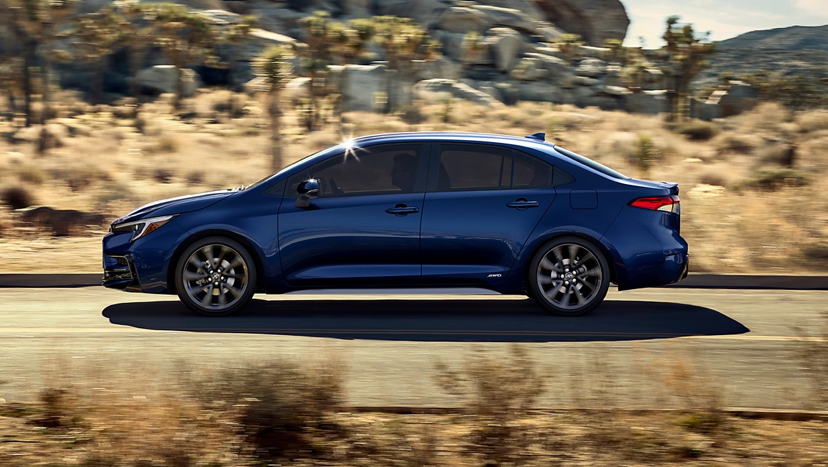 Blue Toyota Corolla sedan driving past a rocky landscape.