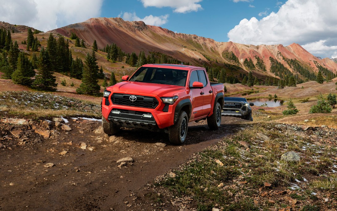 Red Toyota Tacoma with a camping trailer on a mountain trail; Toyota 2024 photography illustrates the 2025 discussion.